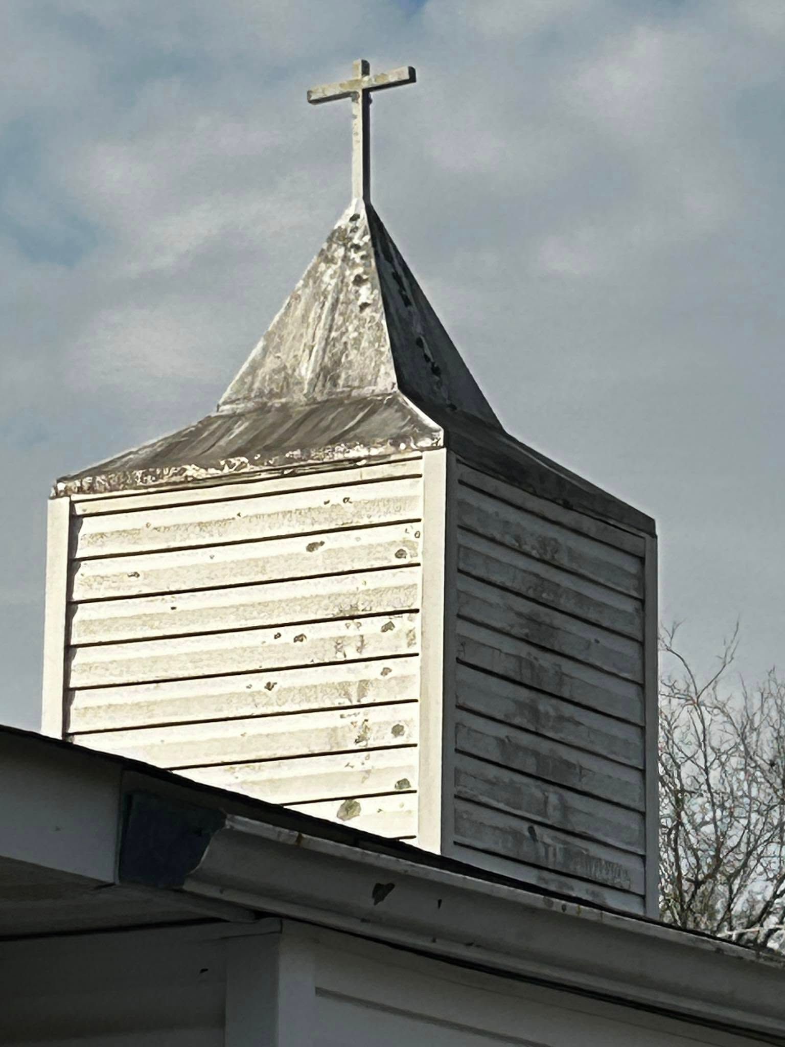 White church steeple with a cross against a cloudy sky