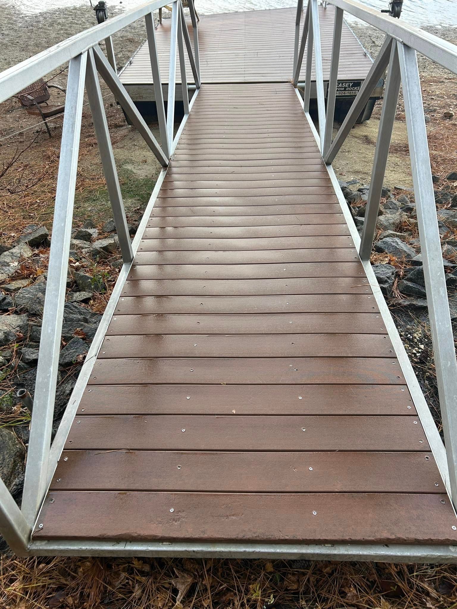 Narrow wooden footbridge with white railings over a rocky shoreline