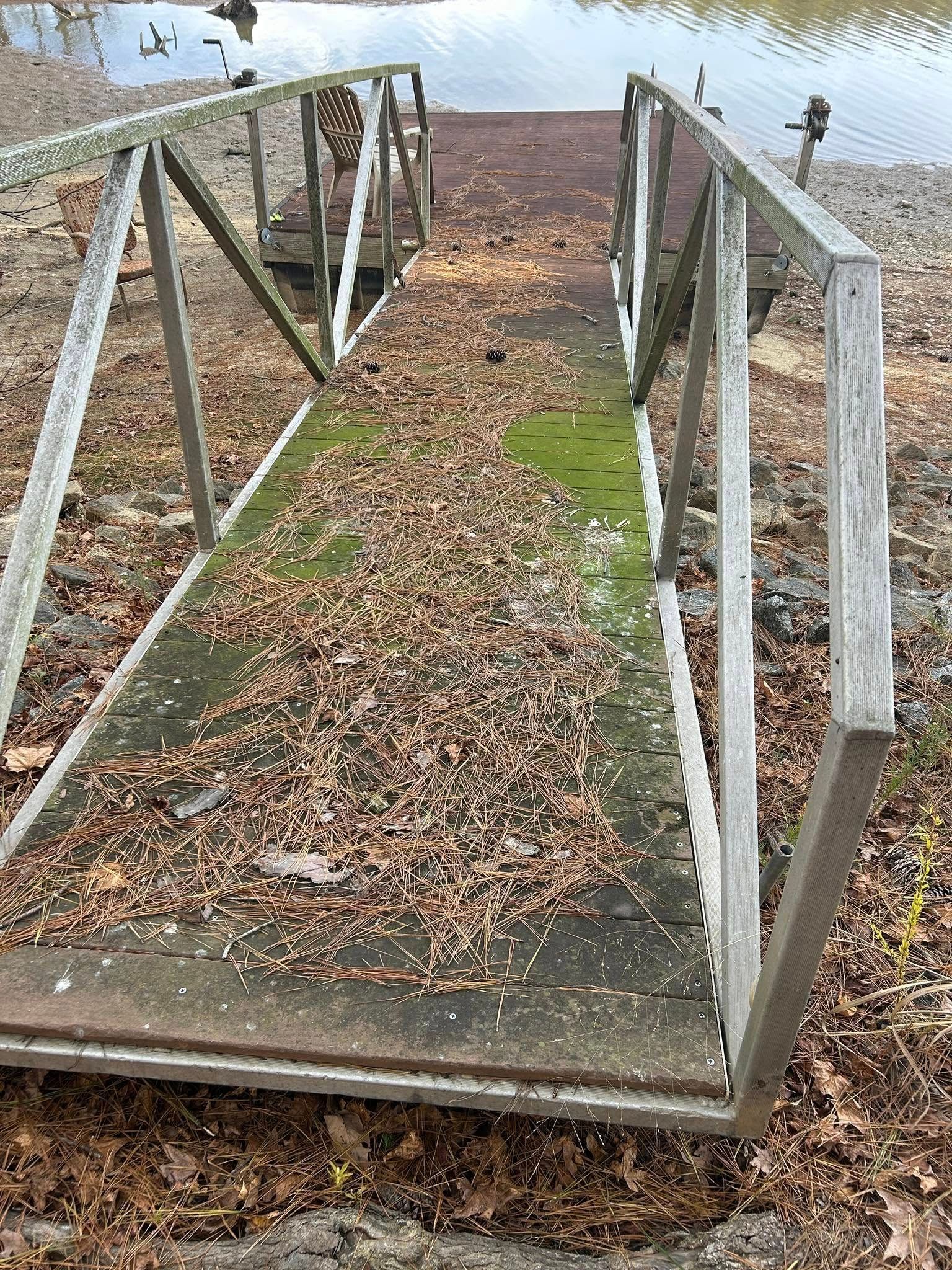 Narrow metal dock ramp covered with fallen leaves leading toward a calm body of water