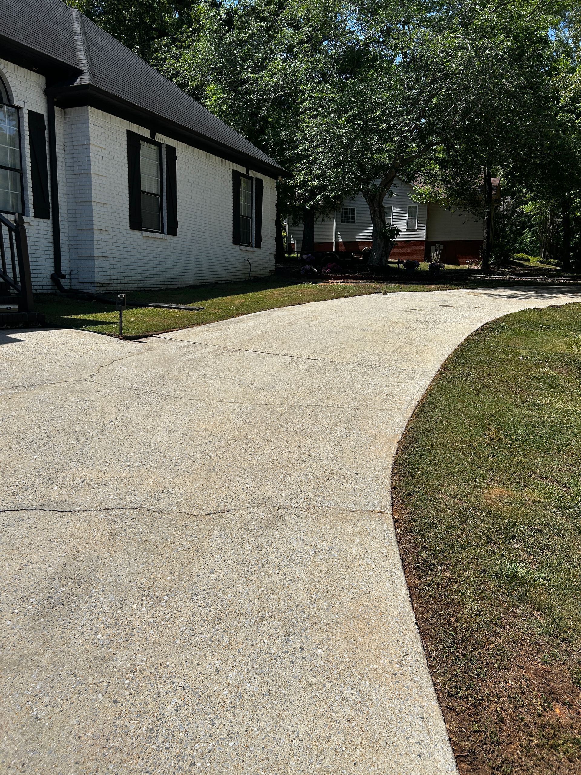 Curved gravel driveway beside a white house and trees on a sunny day