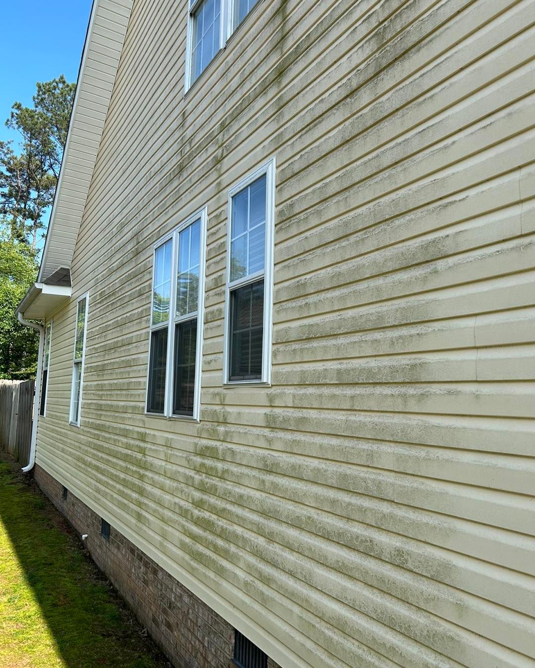Side view of beige house siding with two windows and a narrow grass strip along the foundation