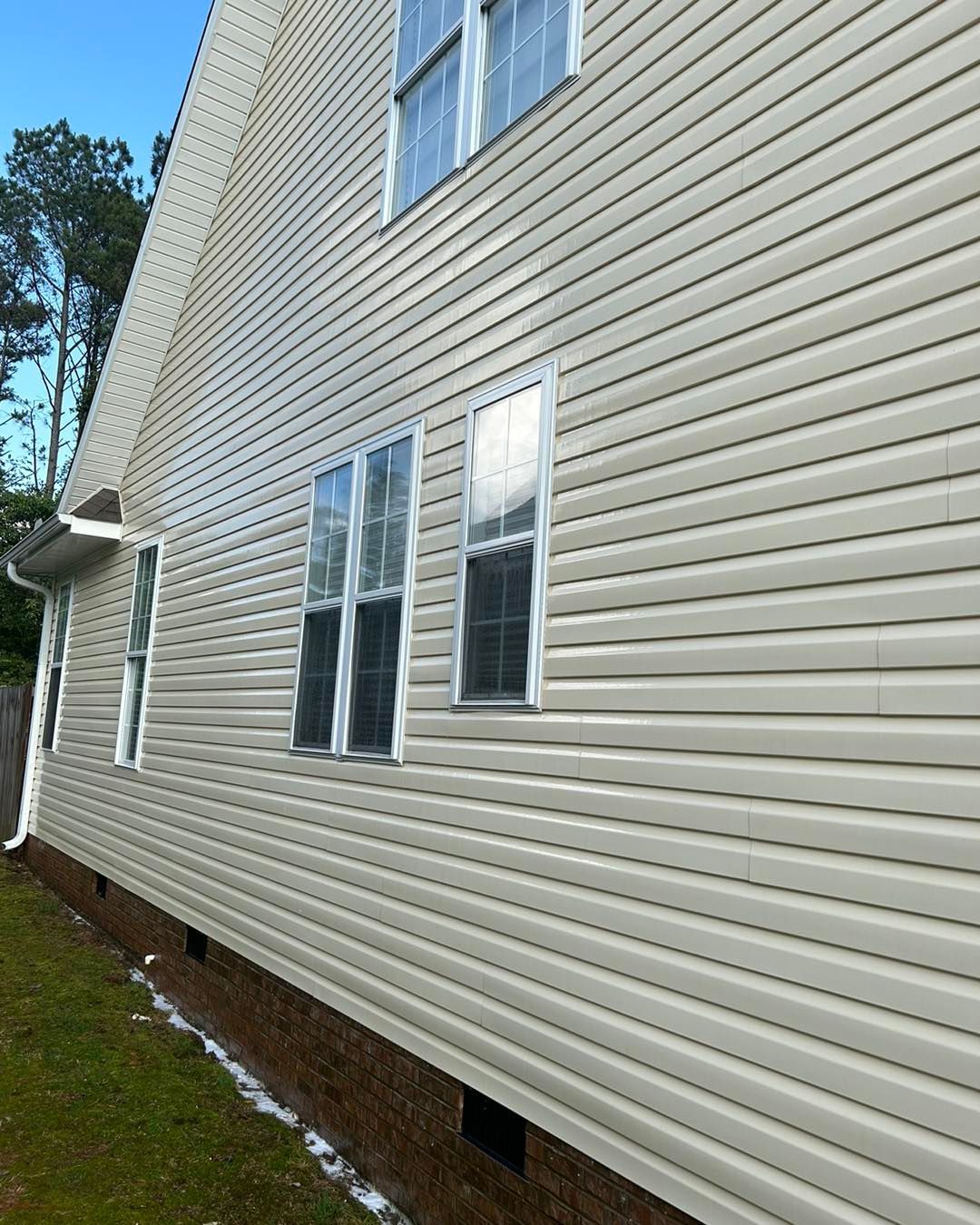 Side of a beige house with vinyl siding and white-framed windows beside a grassy yard.