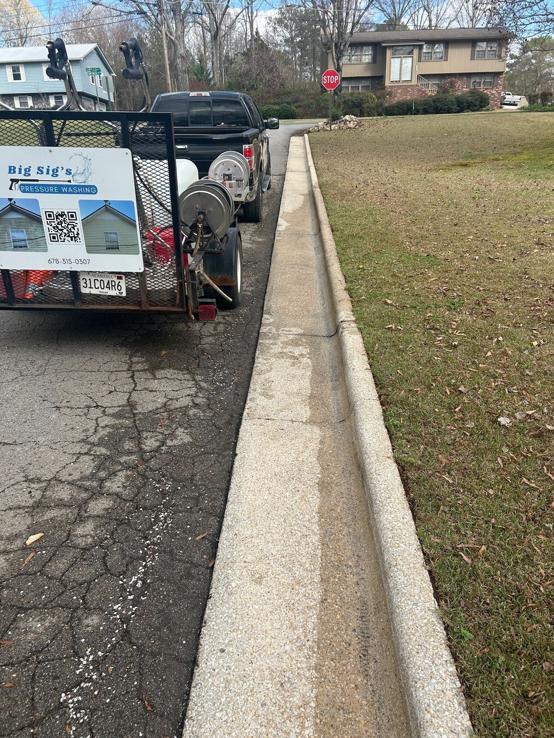 Trailer parked beside a curb ramp along a residential street, with a grassy lawn and houses nearby
