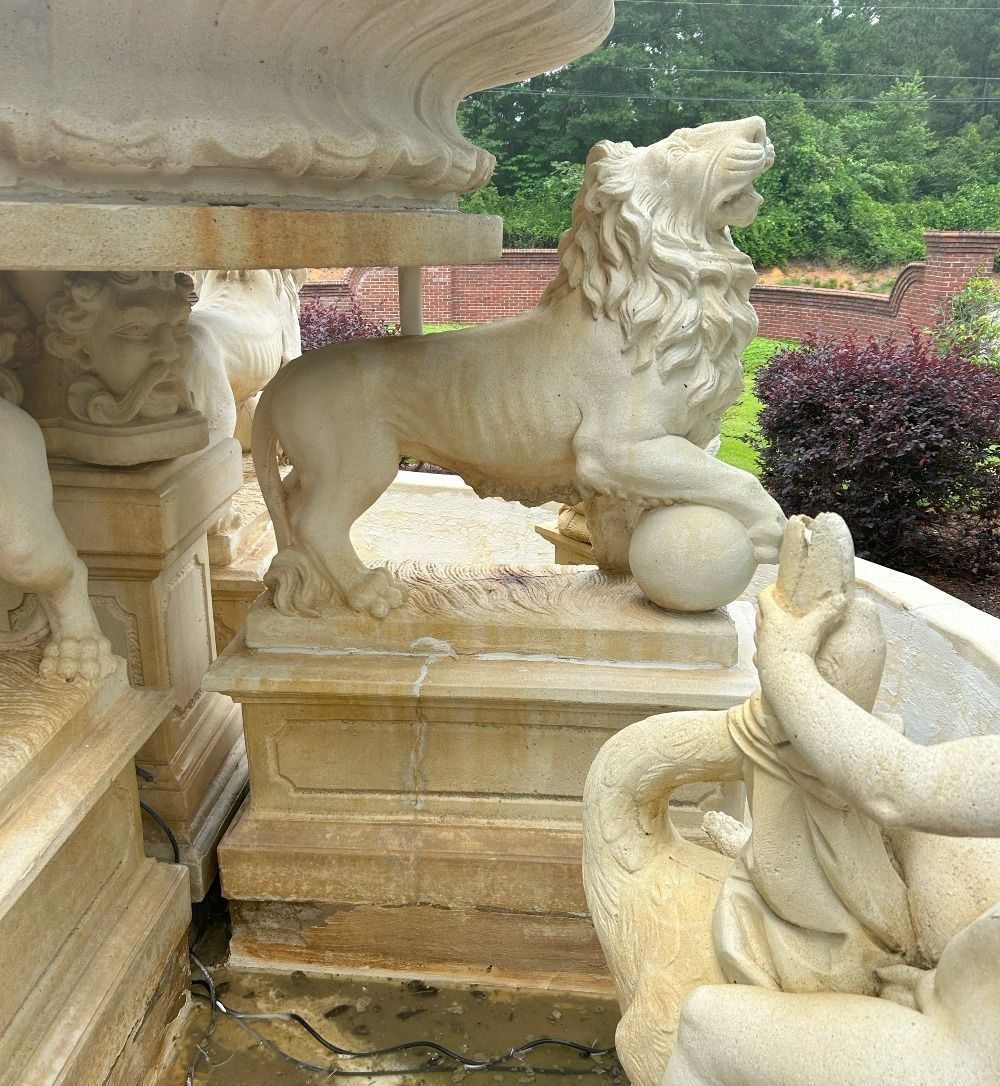 Stone lion statue in a garden, standing on a pedestal beside a fountain