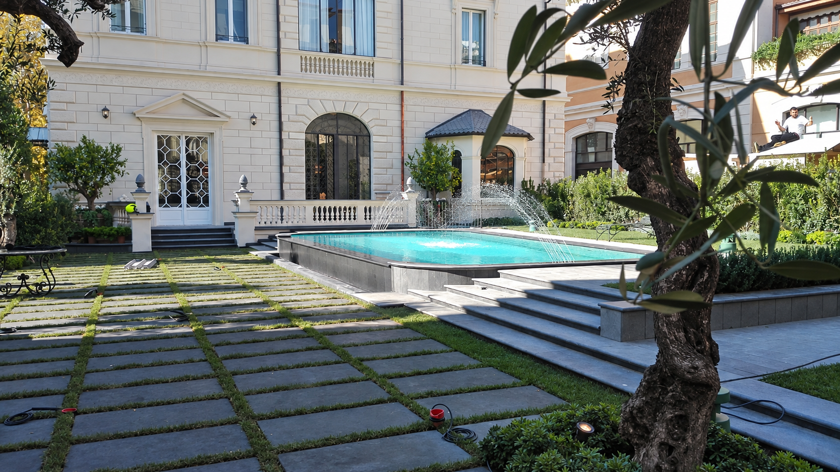 Elegante cortile con una vasca riflettente blu, gradini in pietra, palme e la facciata di un edificio classico