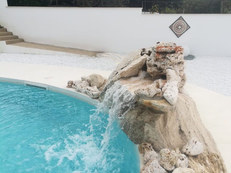 Fontana rocciosa con acqua che si riversa in una piscina turchese accanto a un patio bianco