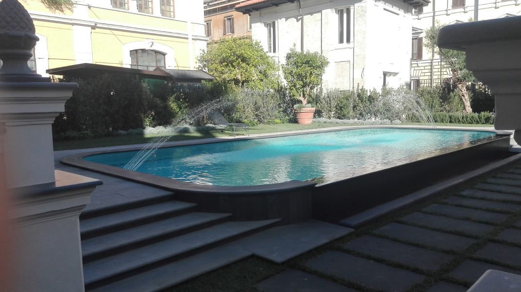 Piscina rettangolare all’aperto con acqua azzurra, circondata da gradini in pietra e da edifici affacciati sul cortile.