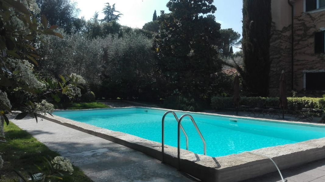 Piscina all’aperto con acqua turchese, bordo in cemento e alberi sullo sfondo