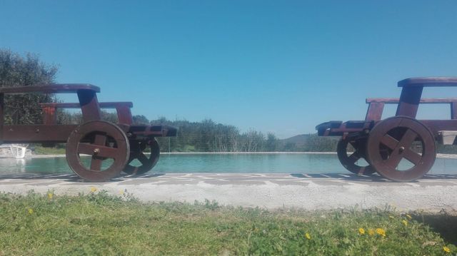 Sculture rustiche di cannoni su una piattaforma di pietra accanto a un lago, sotto un cielo azzurro e terso
