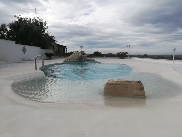 Piscina vuota del resort con acqua turchese, bordo piscina bianco e cielo nuvoloso sulla spiaggia