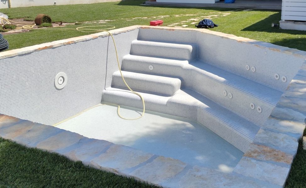 Piscina vuota e bianca con gradini e un tubo dell’acqua nella parte bassa, all’aperto sull’erba