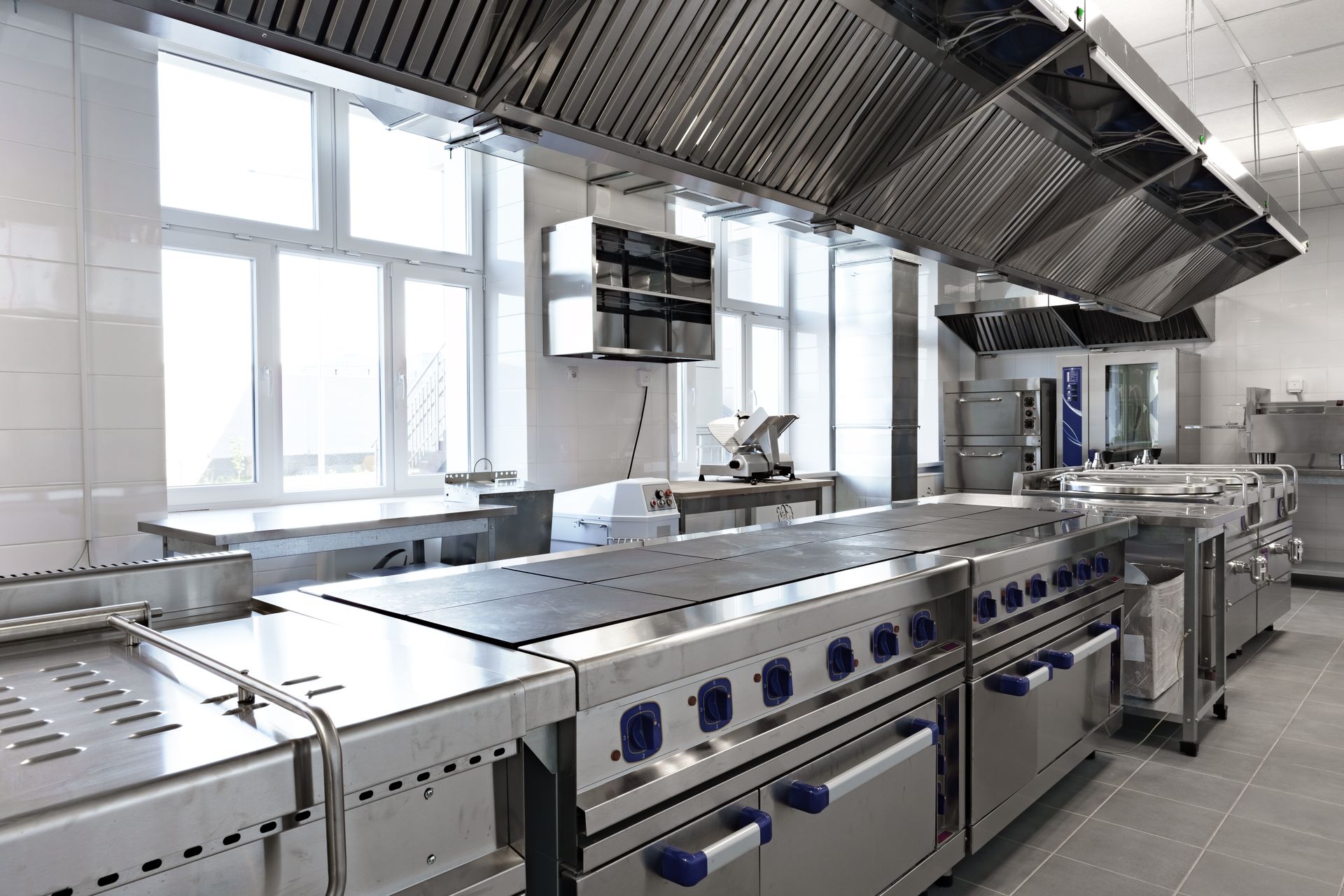 Stainless steel kitchen exhaust hood with vent filters and bright ceiling lights above a tiled wall