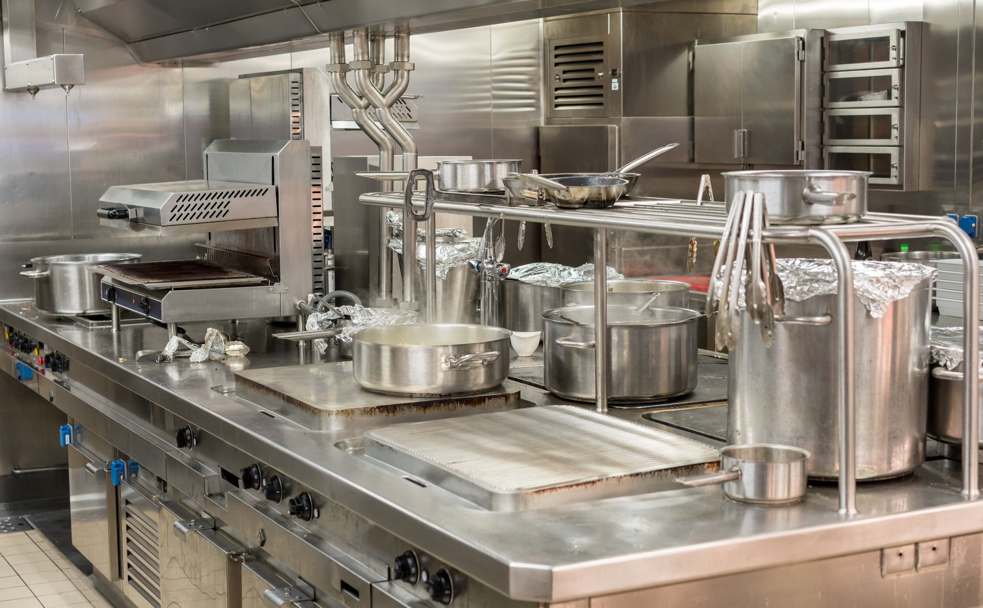 Commercial kitchen line with stainless steel pots, pans, and cookware on counters and stovetops