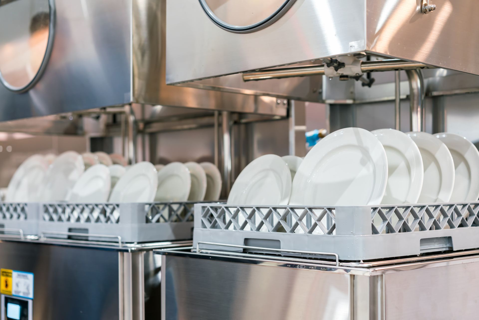 Dish racks with white plates in a stainless steel commercial kitchen dishwasher