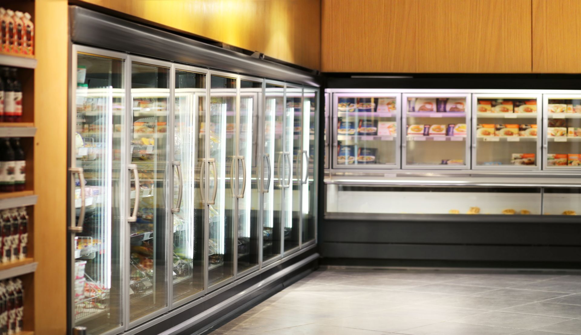 Empty grocery store freezer aisle with glass-door refrigerators and refrigerated display cases on wood-paneled walls