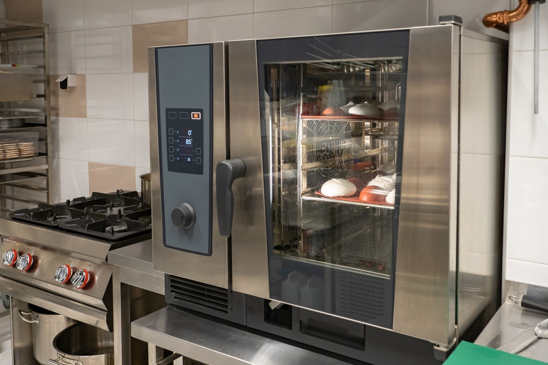 Commercial kitchen with stainless steel oven and a glass-door warming cabinet displaying pastries.