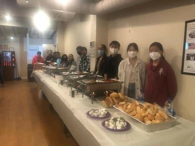 a group of people wearing masks are standing in front of a long buffet table .