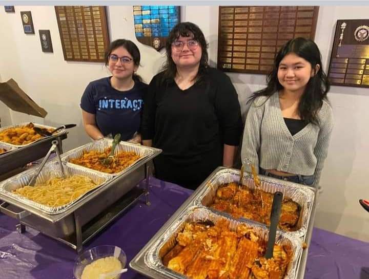 three women are standing in front of a table with trays of food .