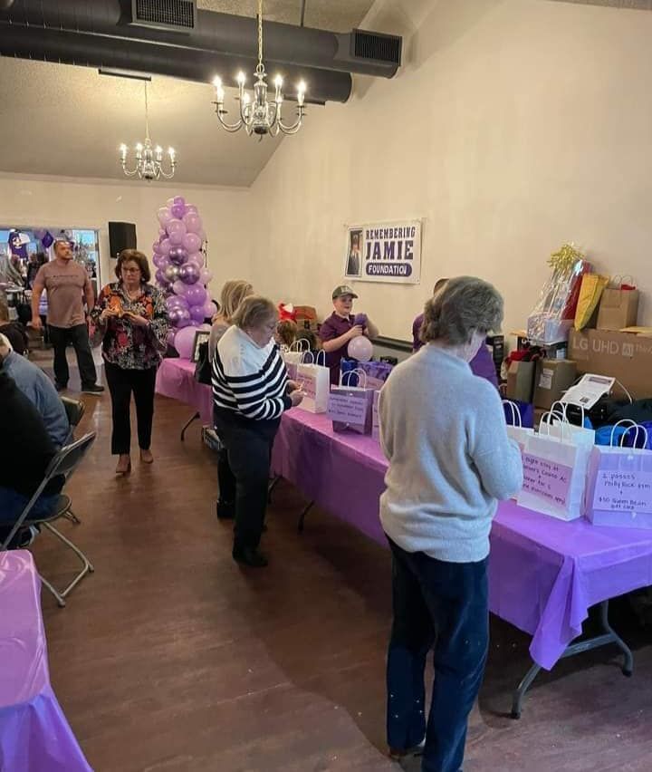 a group of people are standing around tables with purple tables cloths .