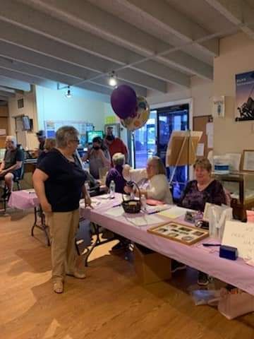a group of people are sitting at tables in a room with balloons hanging from the ceiling .