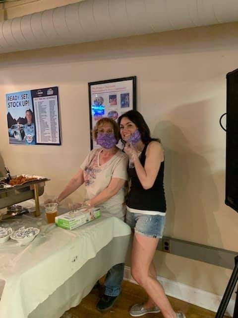 two women wearing masks are standing next to each other in front of a table .