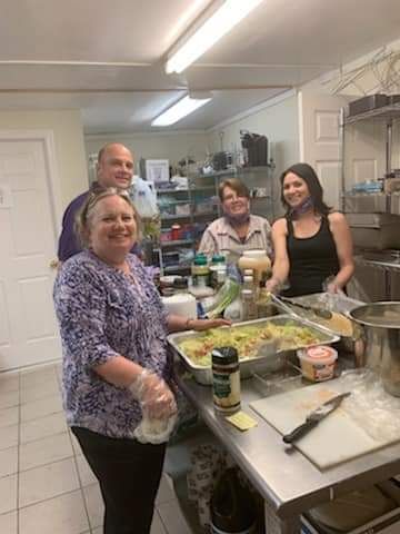 a group of people are standing around a table in a kitchen preparing food .
