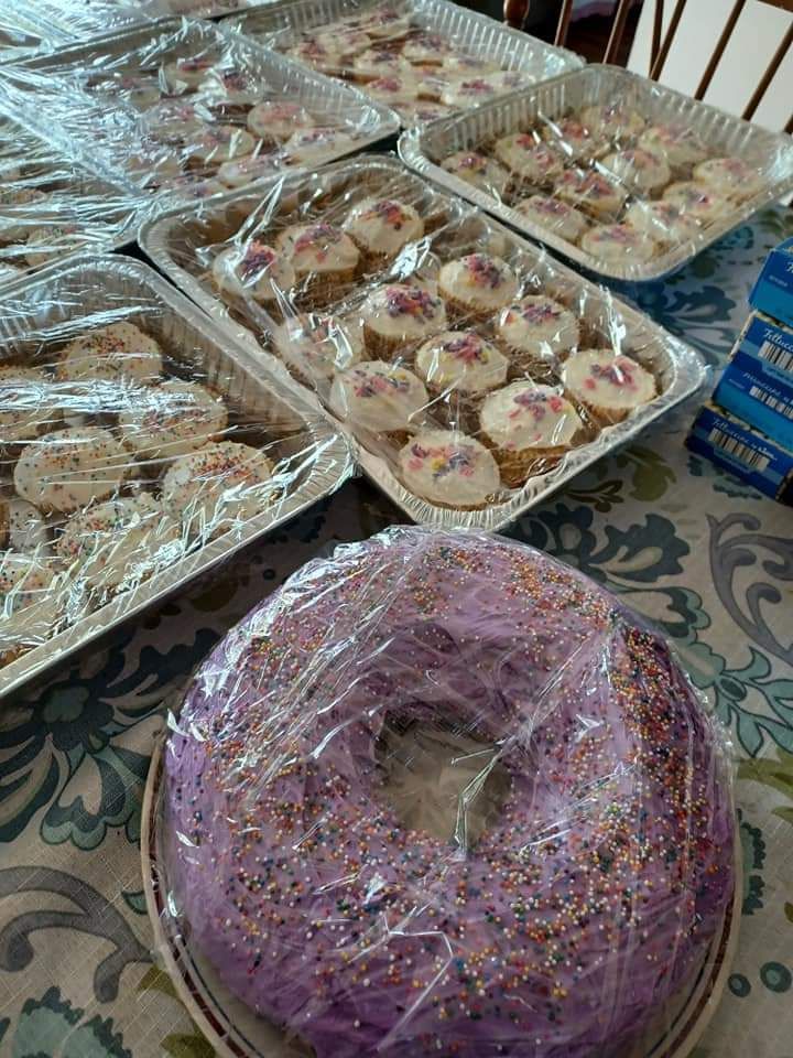 a purple cake is sitting on a table next to a bunch of cookies .