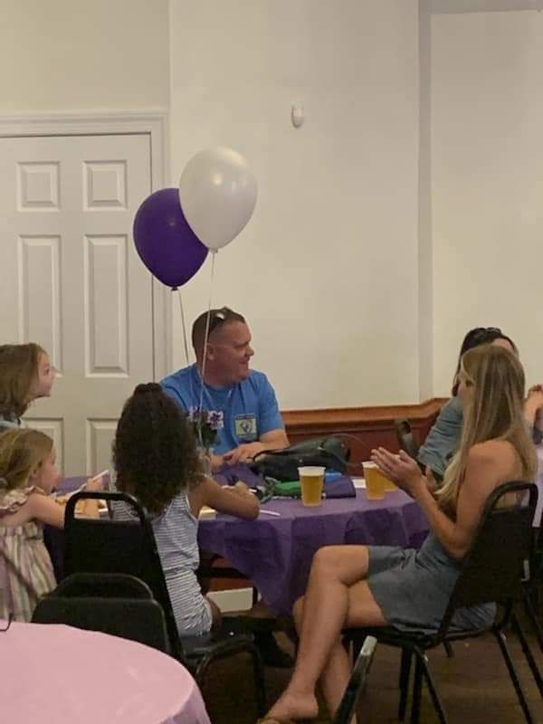 a group of people are sitting at tables with balloons hanging from the ceiling .