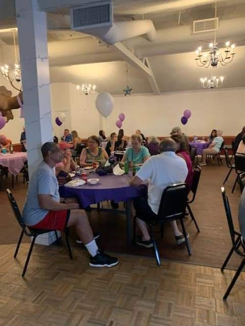a group of people are sitting at tables in a room with balloons hanging from the ceiling .