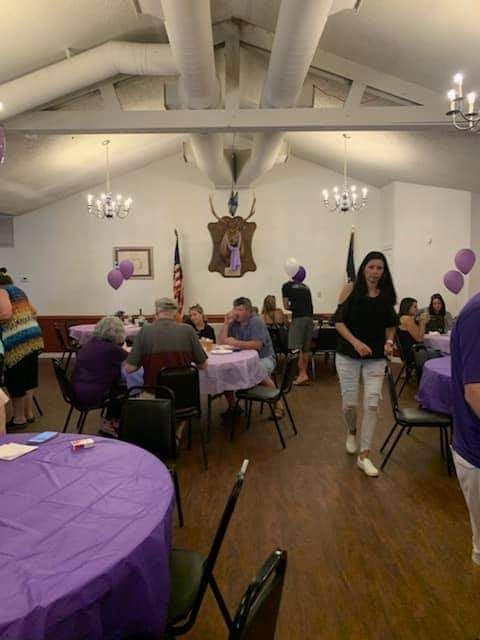 a group of people are sitting at tables in a room with purple tables and chairs .
