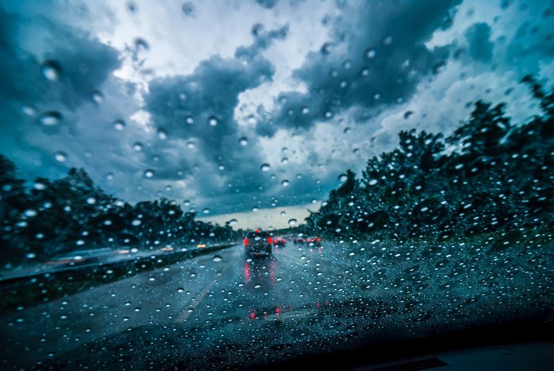 Raindrops on windshield, blurred view of road with cars, dark cloudy sky