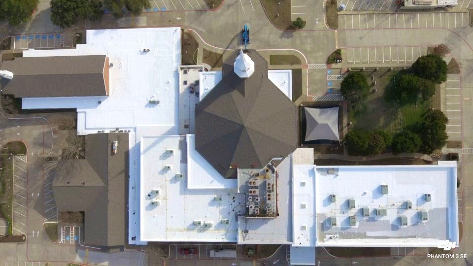 Aerial view of a church with multiple buildings, white roofs, and a central octagonal dark brown roof.