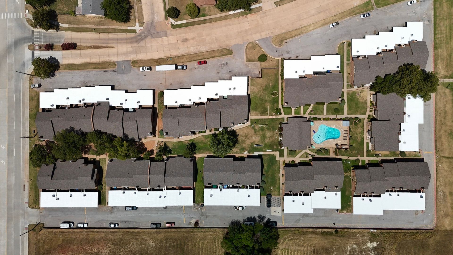 Aerial view of an apartment complex with brown roofs, white accents, a pool, and parking areas.