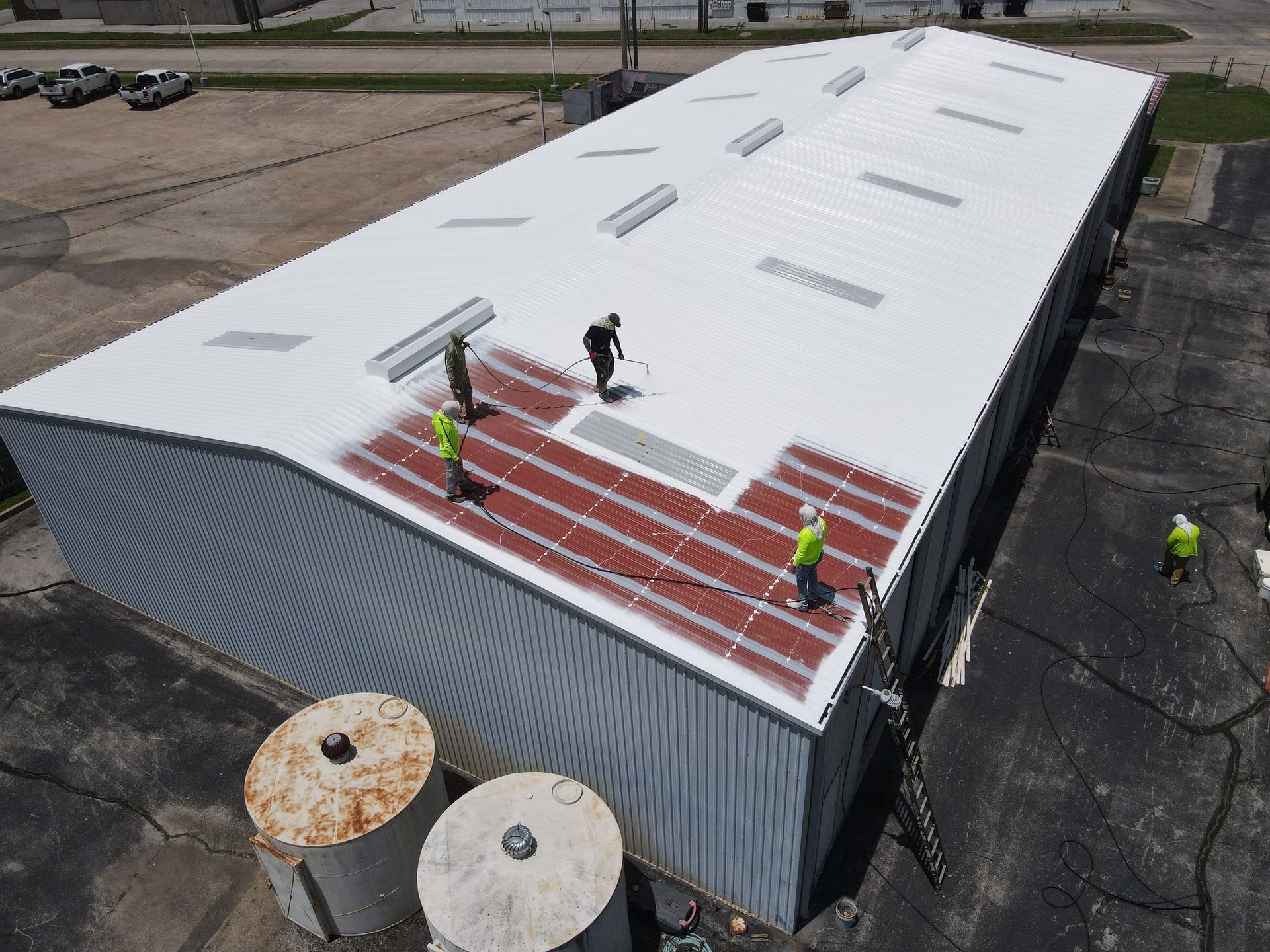 Workers on a white industrial building roof installing red panels.