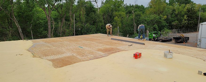 Construction workers installing roofing on a building's rooftop, surrounded by trees.