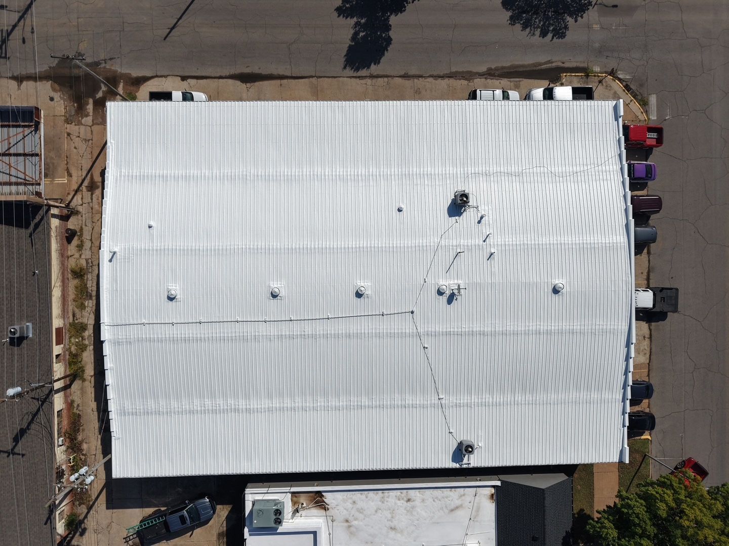 Aerial view of a large white-roofed building with people around the edges and parked cars nearby.
