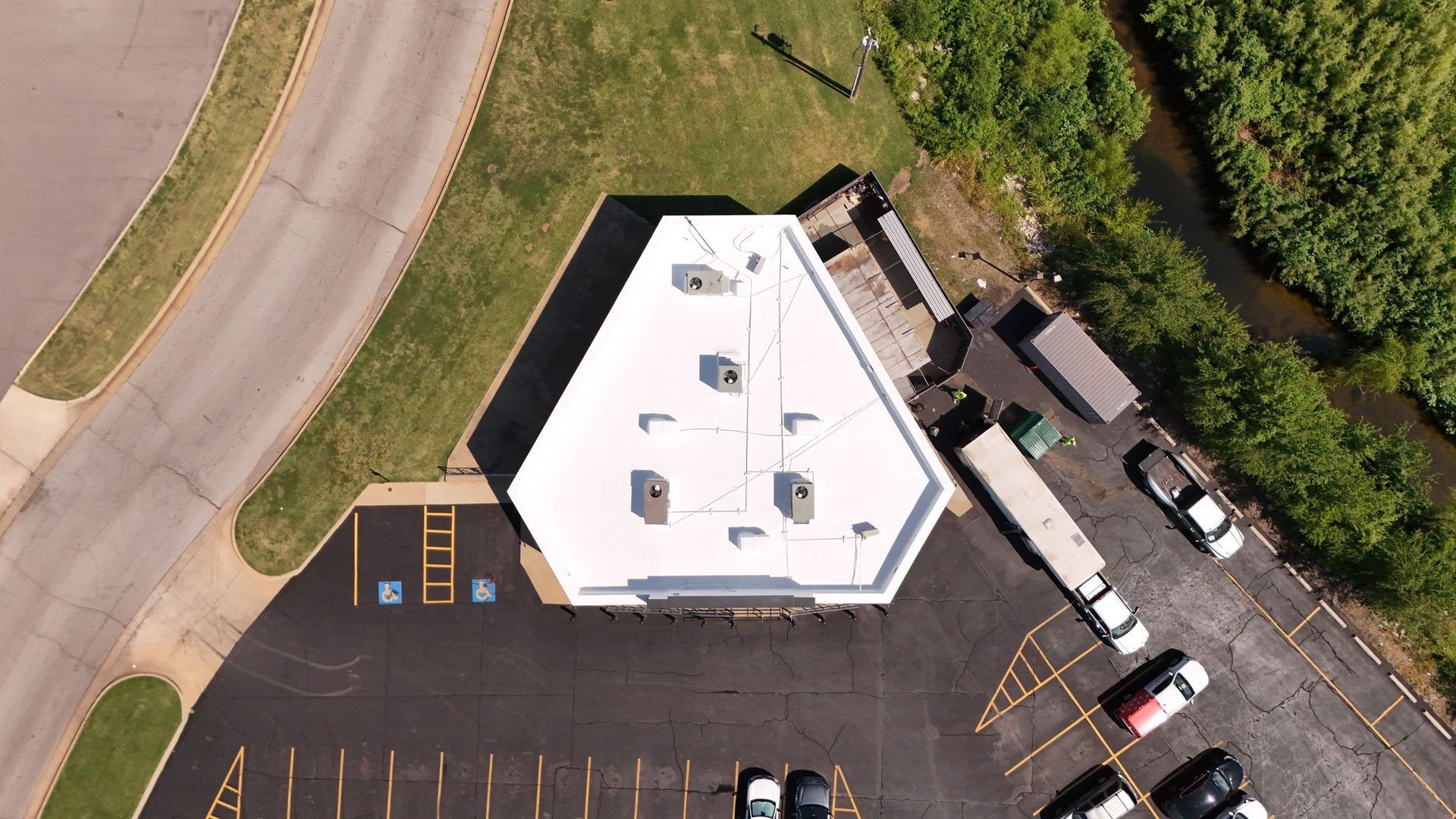 Aerial view of a white, pentagonal building with HVAC units on its roof, surrounded by a parking lot and grassy areas.