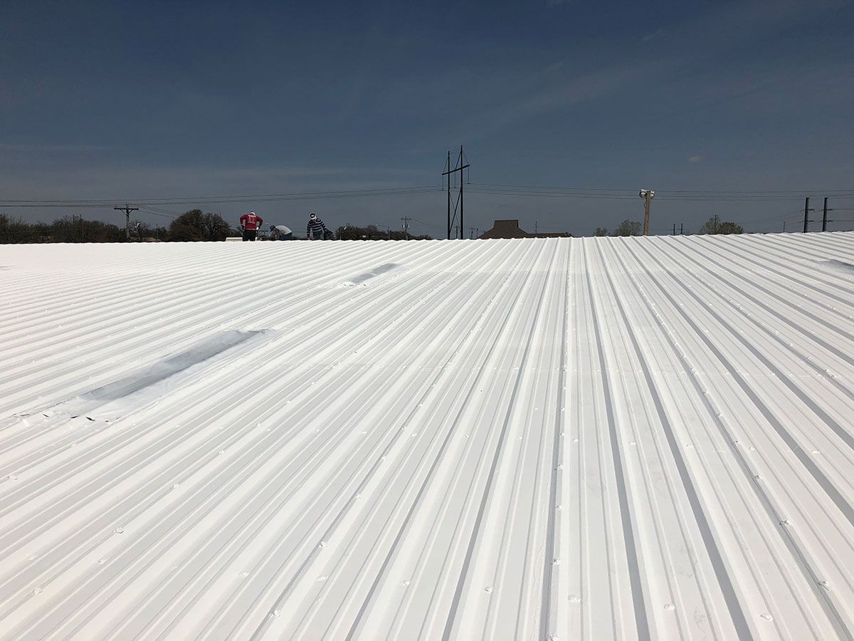 Aerial view of a white commercial flat roof with equipment, adjacent to a parking lot.