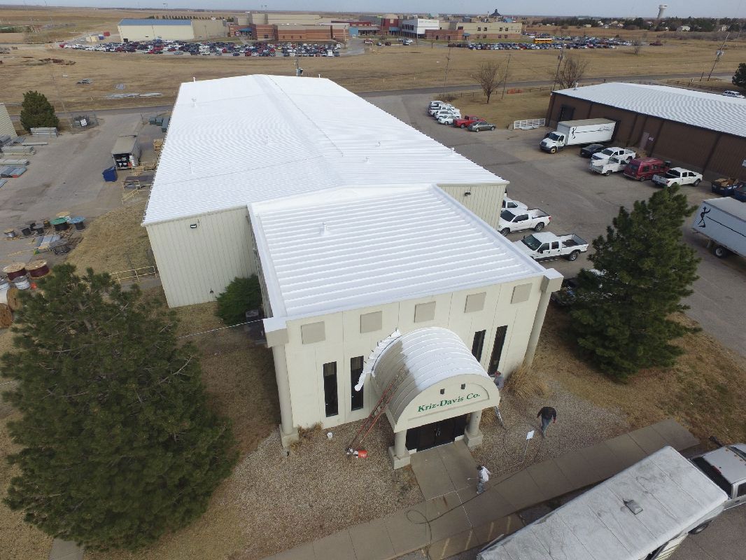 Aerial view of a light-colored building with a white roof, surrounded by parking and industrial areas.
