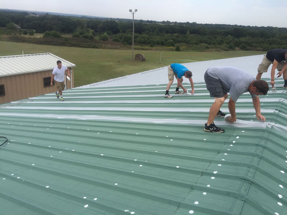 Men repairing a green metal roof on a building outdoors.