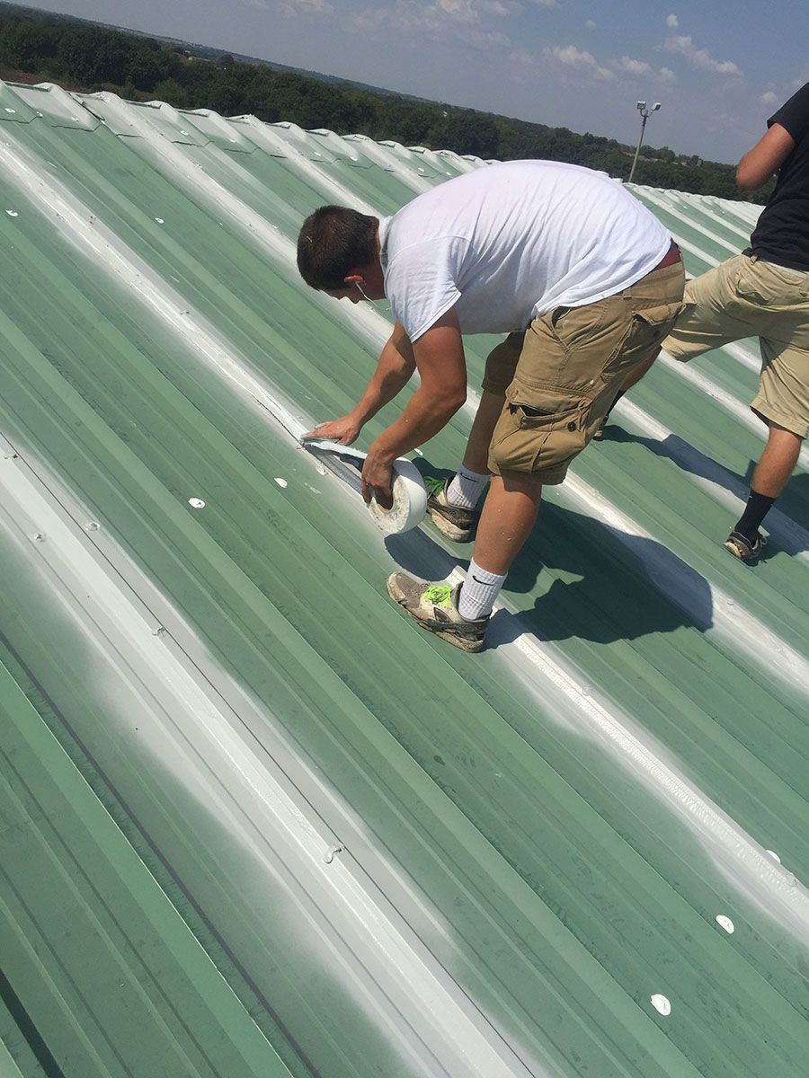 Two men on a green metal roof, one is sealing a seam. Sunny day.