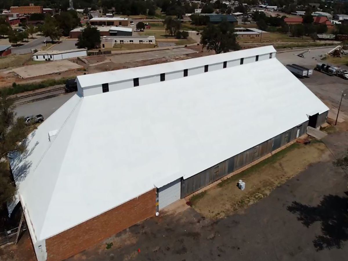 Aerial view of a large white-roofed building in a small town setting, with a few buildings in the background.