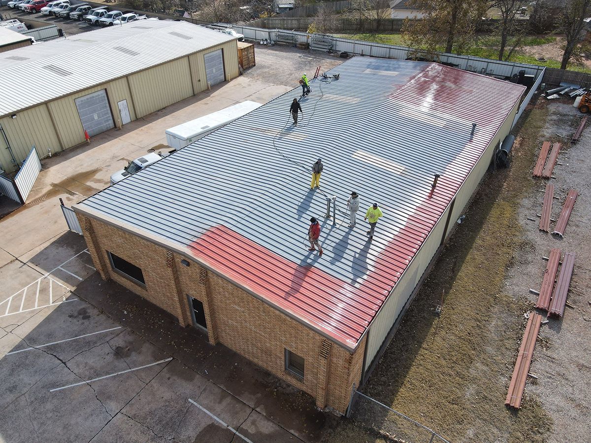 Workers install a curved, red-and-white patterned roof covering on a flat-roofed commercial building.