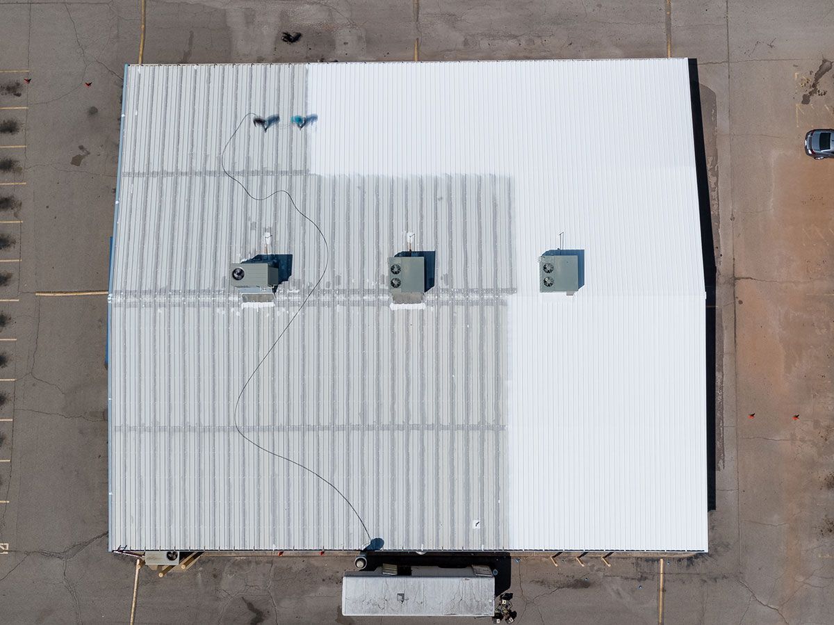 Overhead view of a white industrial building with AC units and a corrugated metal roof.