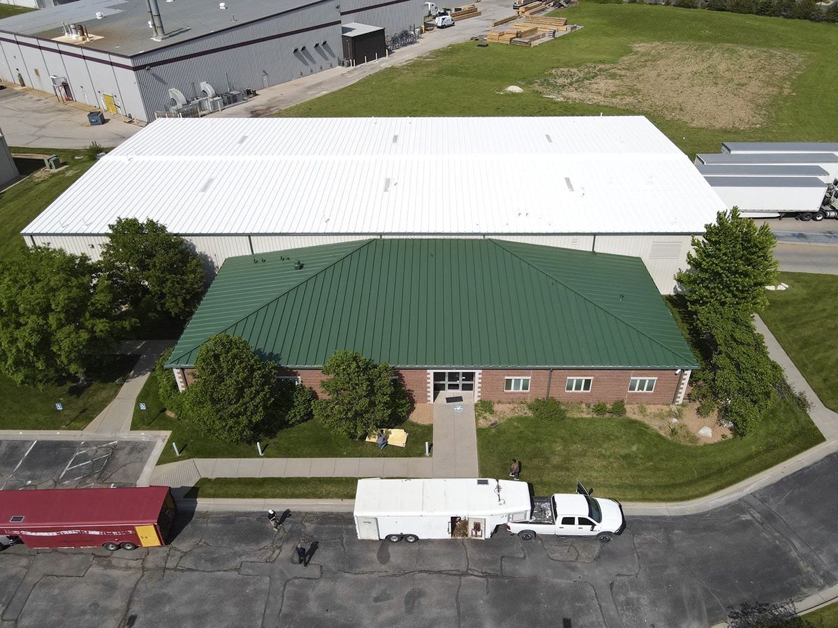 An aerial view of a brick office building with a green roof, attached to a large warehouse with a white roof.