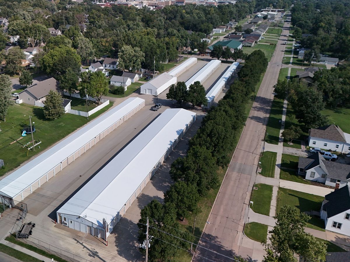 Aerial view of storage units along a street lined with trees, near residential homes.