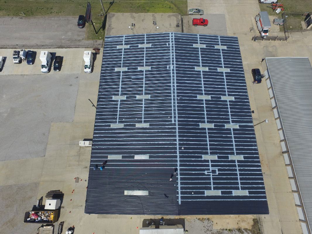 Aerial view: Workers installing solar panels on a large commercial building roof.