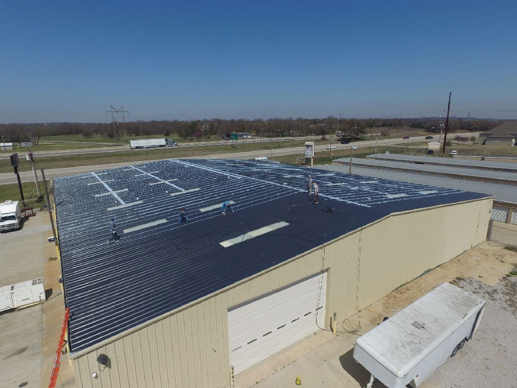 Large commercial building with dark gray roof, blue sky, and surrounding rural area.