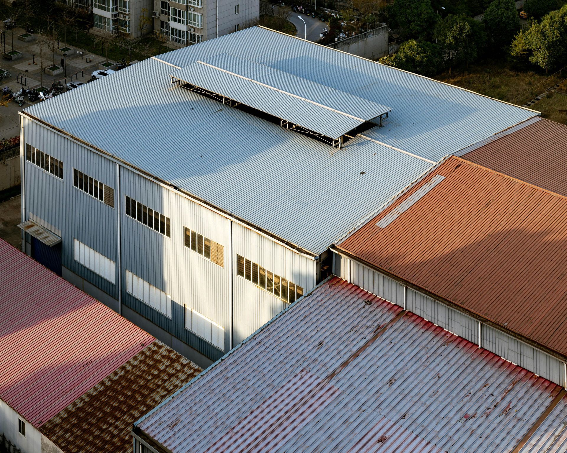 Aerial view of white corrugated-roof warehouse beside red-roofed buildings.