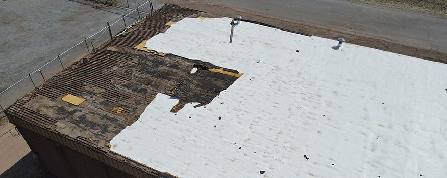 Aerial view of a building roof with damaged areas and a white covering.
